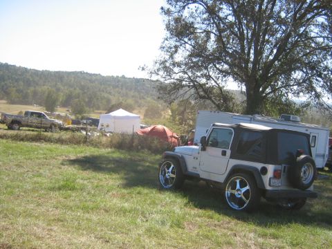 1986 Ford Bronco - A white Jeep Wrangler with large chrome rims is parked in a grassy area next to a trailer.