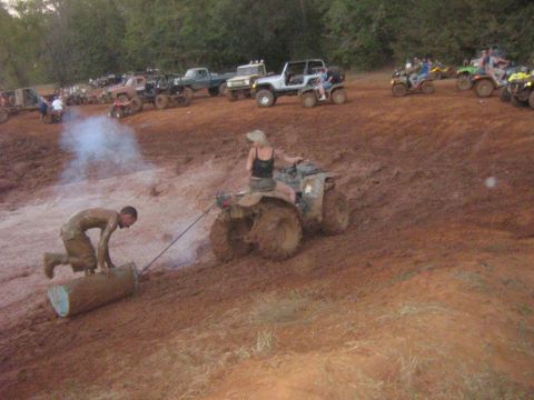 1986 Ford Bronco - Multiple ATVs and trucks are gathered in a muddy outdoor area, with people interacting with the terrain.