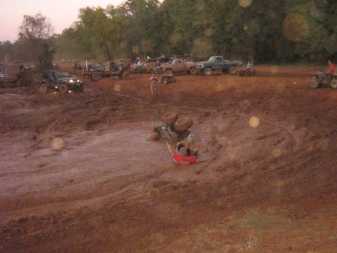 1986 Ford Bronco - A group of off-road vehicles and people are gathered in a muddy area, with some vehicles stuck in the mire.