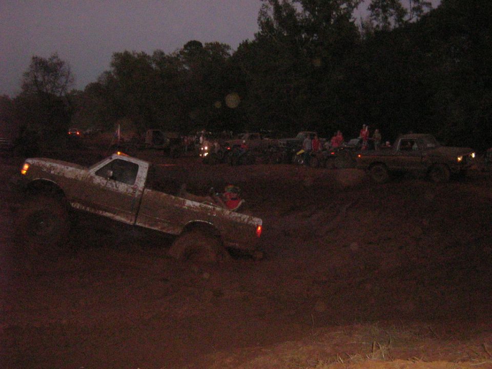Mud-covered white Ford F-Series truck stuck in mud, side view