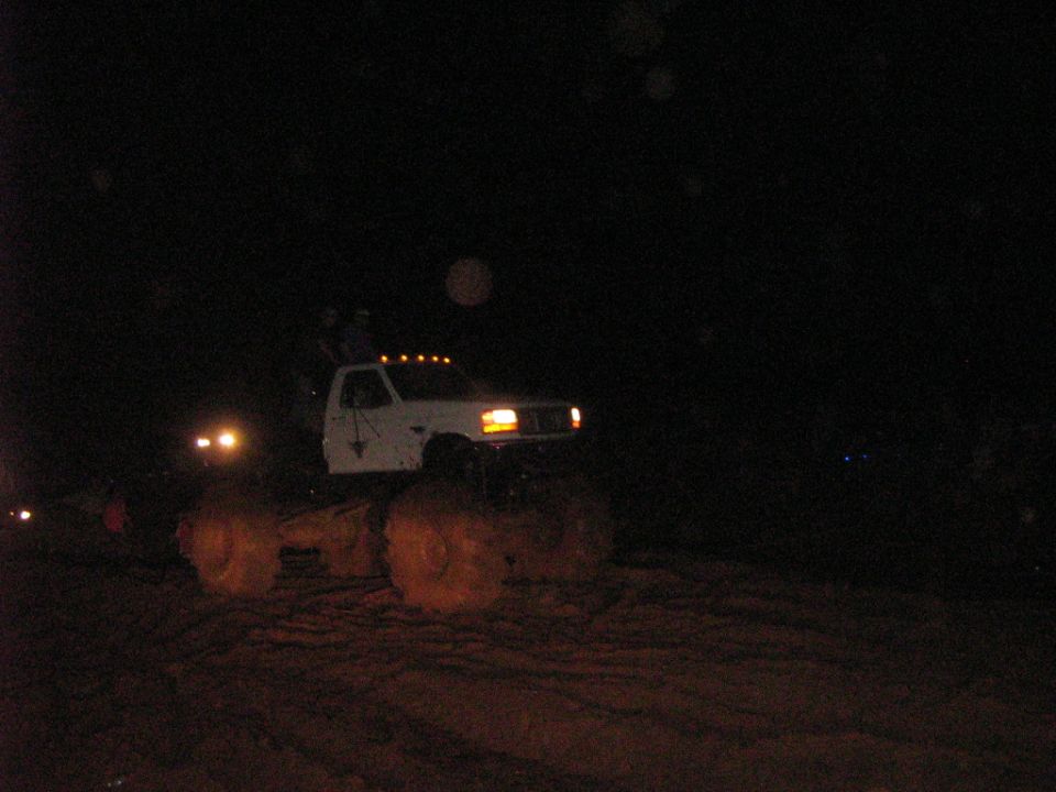 White Ford mud truck on huge flotation tires at night with cab marker lights glowing
