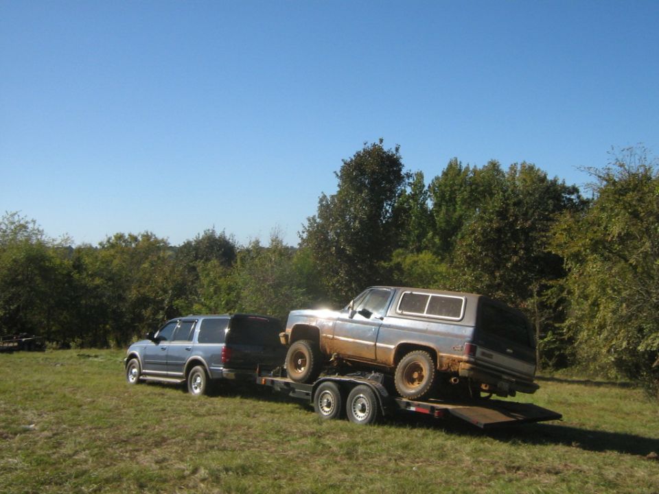Blue SUV towing a trailer with a muddy older SUV on it