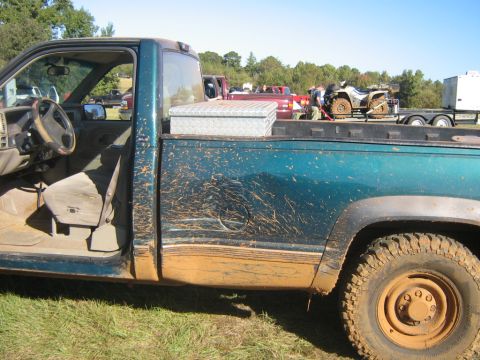 1986 Ford Bronco - Mud-splattered teal pickup truck seen from the side, with a toolbox in the bed and an ATV on a trailer in the background.