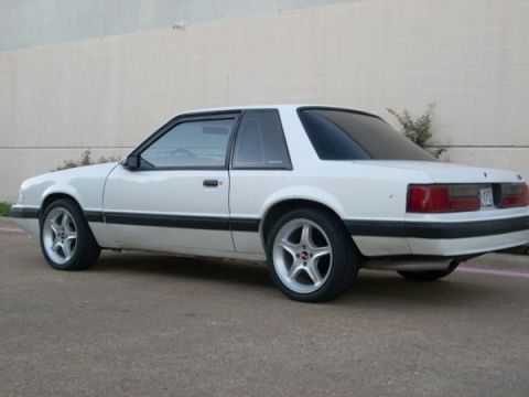 1991 Ford Mustang - A white 1991 Ford Mustang coupe is shown from the rear three-quarter angle, aftermarket wheels and black trim.