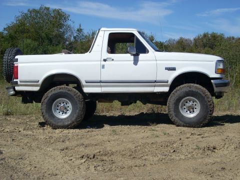 1992 Ford Bronco - This 1992 Ford Bronco is shown from the side, parked on a dirt road with trees and a blue sky overhead.