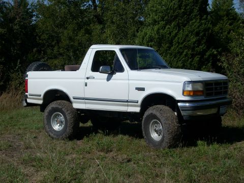 1992 Ford Bronco - This lifted 1992 Ford Bronco is shown in a three-quarter front view, parked outdoors on grassy terrain.