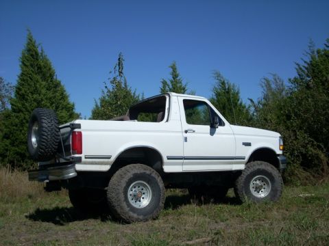 1992 Ford Bronco - A white 1992 Ford Bronco is parked outdoors on a sunny day, with trees and foliage in the background.