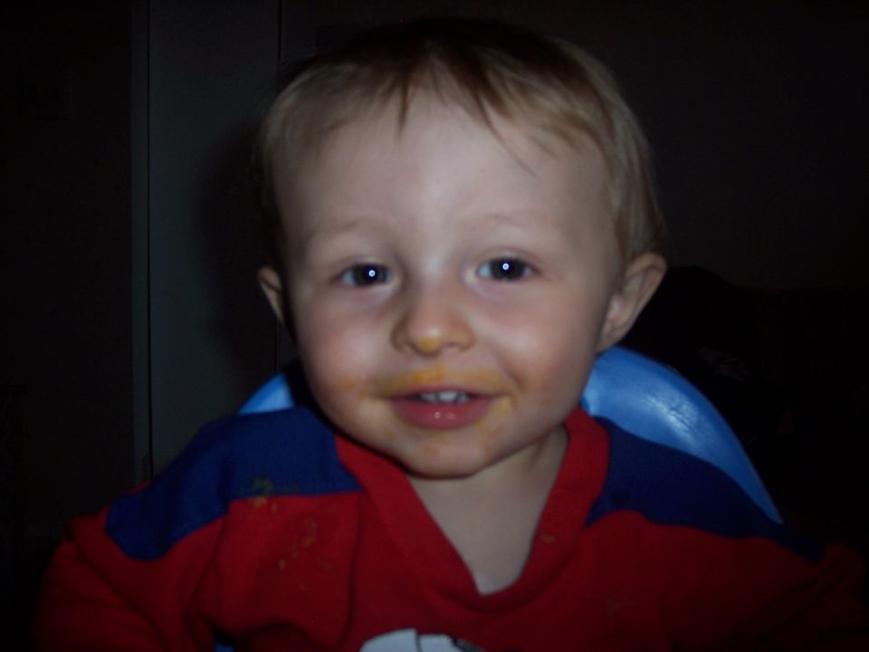 Toddler with orange food around mouth, wearing a red and blue shirt