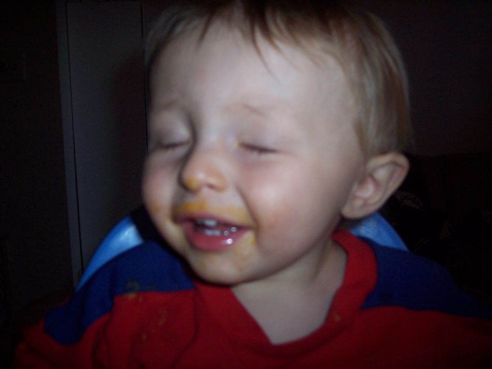 Toddler with eyes closed and food smeared around mouth, wearing a red and blue shirt