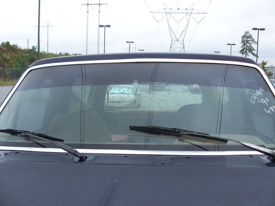 Cracked windshield of dark 1990 Ford Bronco with grease-pencil markings, viewed from the front over the hood