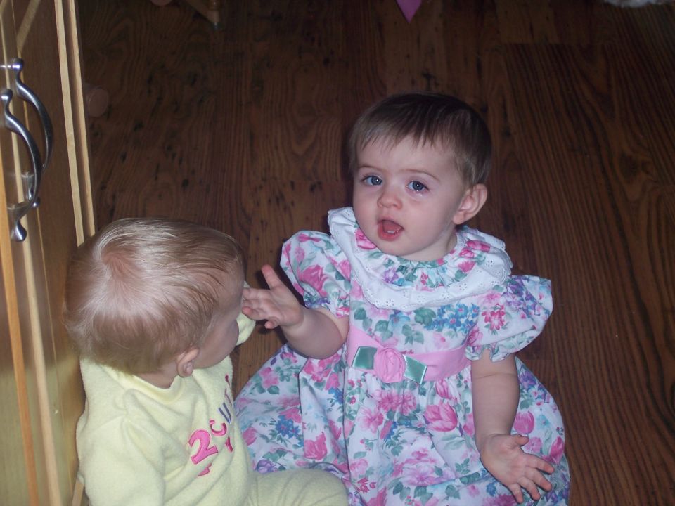 Two babies on a wooden floor, one in a floral dress