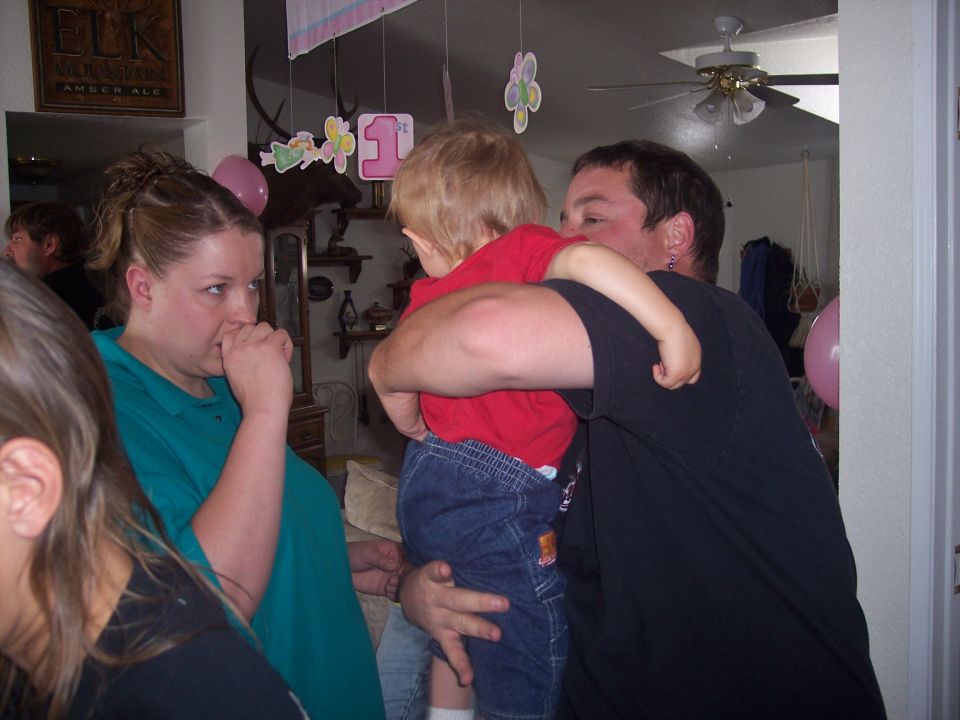 Woman in teal shirt looks away while man holds a toddler. Decorations hang from the ceiling