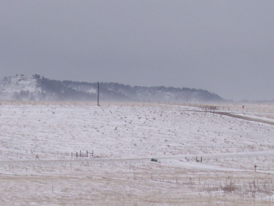 Snowy field with a dirt road and a distant green car