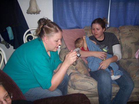 1972 Ford Ranchero - A woman uses a digital camera to photograph a baby being held by another woman on a couch, with blue curtains in the background.