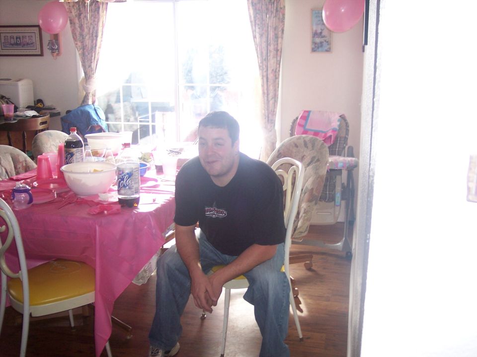 man sitting at a table with pink tablecloth, balloons, and drinks