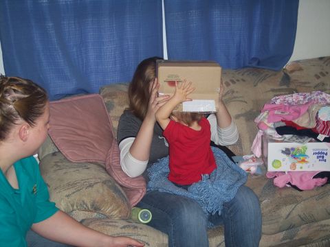 1972 Ford Ranchero - A child playfully hides their face behind a cardboard box while sitting on a woman's lap on a couch.