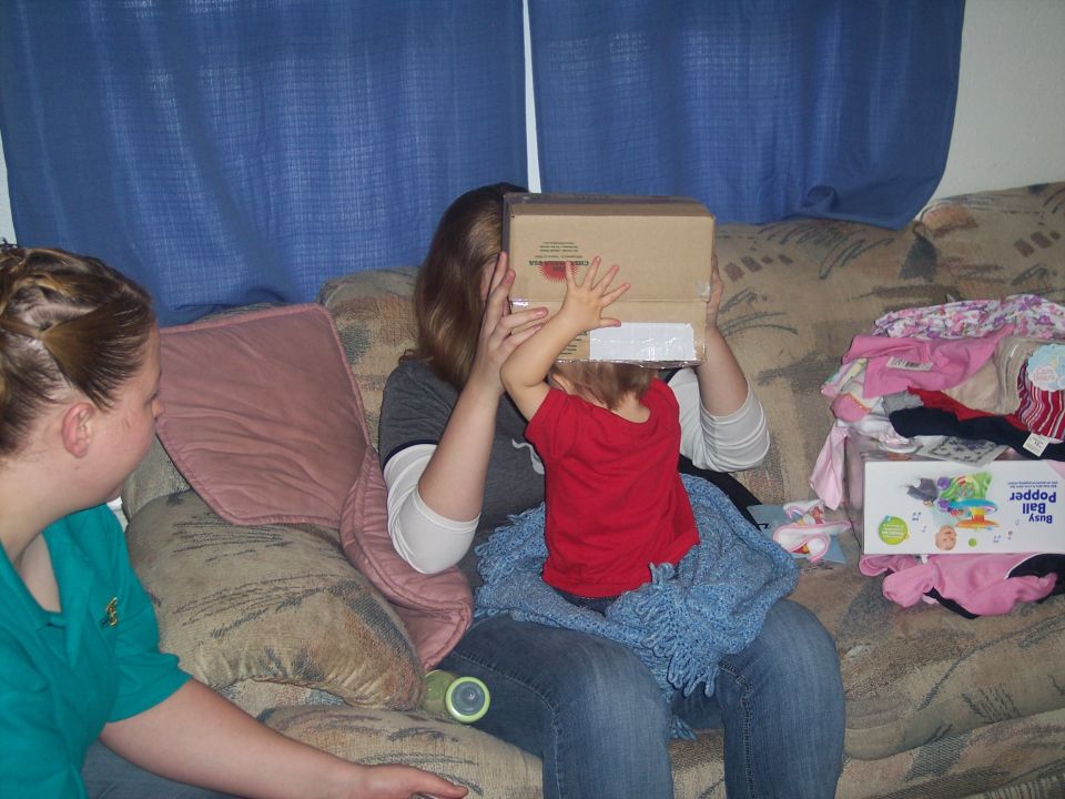 Woman and child on couch, child holding box over face