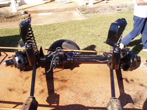 1980 Ford Bronco - A person is working on a vehicle's front axle assembly, which is resting on a metal surface outdoors.