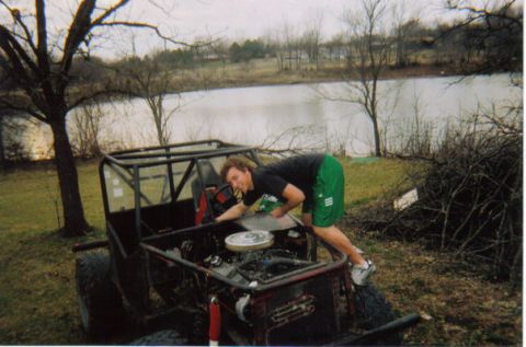 1994 Ford Bronco - A person works on the engine of an off-road buggy near a body of water.