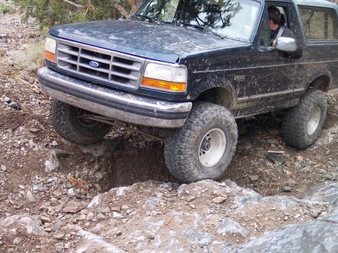 1995 Ford Bronco - A 1995 Ford Bronco tackles a challenging off-road obstacle with its front tire dropping into a crevice.