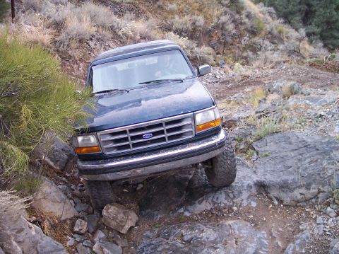 1995 Ford Bronco - A dark blue SUV navigates a challenging rocky terrain on an off-road trail.