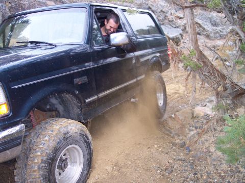 1995 Ford Bronco - A man drives a black Ford Bronco off-road, navigating a rocky, dusty path.