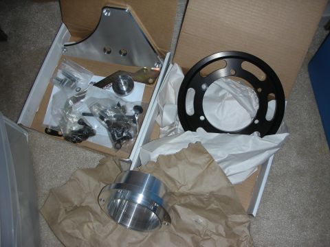 1998 Ford Crown Victoria - Open shipping box holding machined aluminum spacer rings, a bracket and bags of bolts and hardware on carpet.
