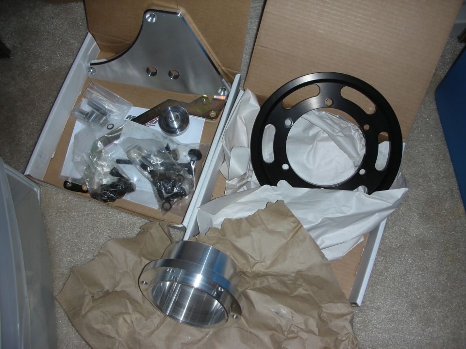 Cardboard box of machined aluminum and black metal parts with brackets and hardware