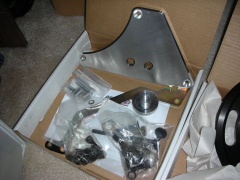 1998 Ford Crown Victoria - Shipping box with a large polished aluminum mounting bracket, a steel spacer and several bags of black bolts and parts.