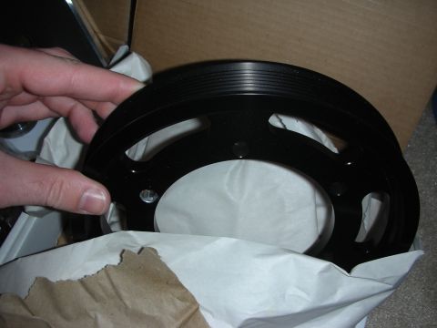 1998 Ford Crown Victoria - hand holds a black grooved aluminum ring pulley over a cardboard box lined with white and brown packing paper.