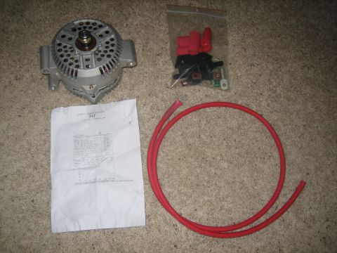 1995 Ford Bronco - High-output alternator upgrade kit laid out on tan carpet: a bare cast-aluminum alternator, a bagged wiring harness with red insulated term…