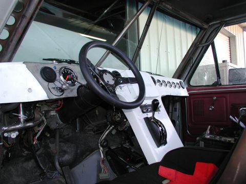 1980 Ford Bronco - Vehicle interior with custom dashboard, steering wheel, and shifter; roll cage is installed.