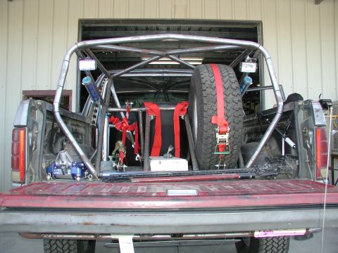 1980 Ford Bronco - The bed of a pickup truck is outfitted with a custom roll cage and a secured spare tire.