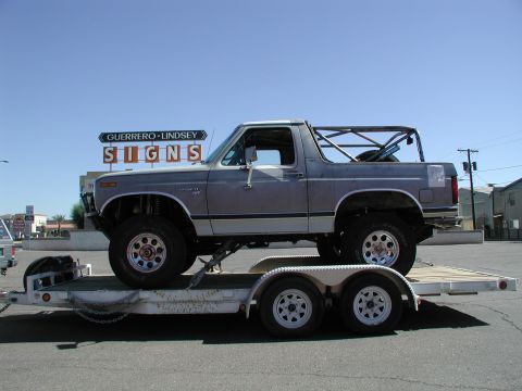 1980 Ford Bronco - A lifted 1980 Ford Bronco with a roll cage is transported on a trailer under a clear blue sky.