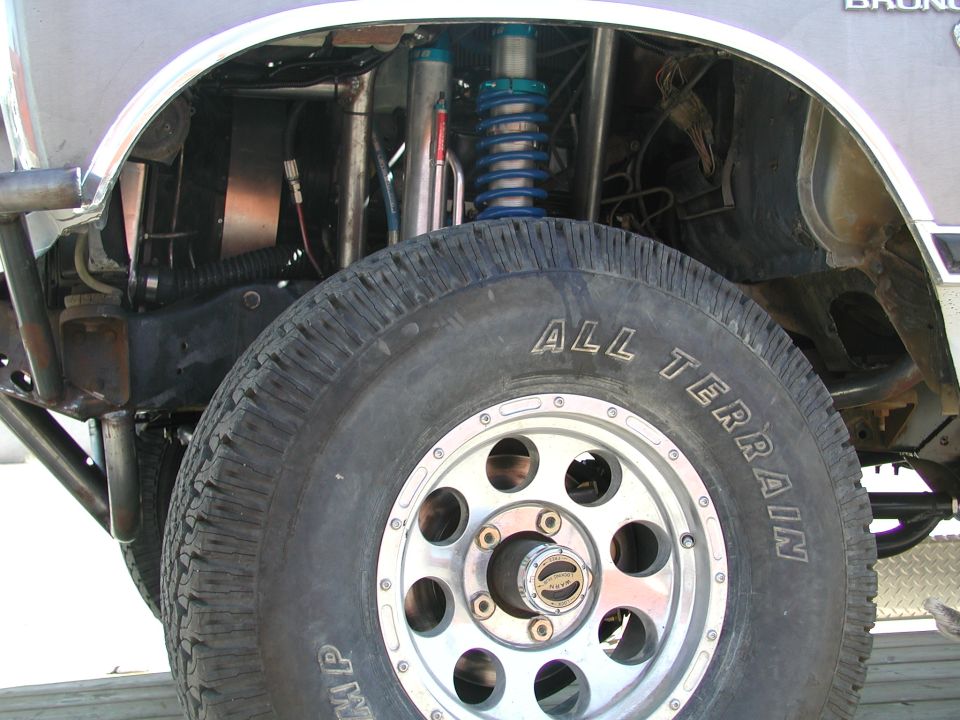 Close-up of a modified off-road suspension system on a vehicle, showing a large tire and custom shocks