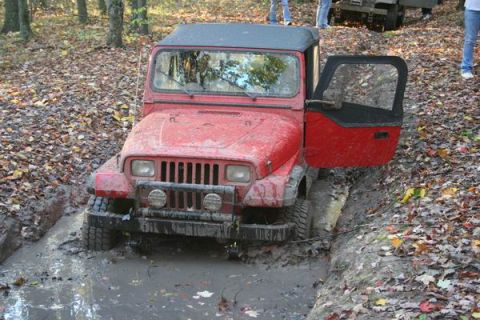 1992 Jeep Cherokee - A red Jeep Wrangler navigates a muddy off-road trail, its door ajar.