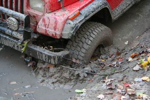 1992 Jeep Cherokee - A red Jeep Cherokee is stuck in thick mud, with its front tire deep in the mire.