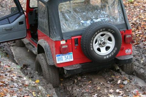 1992 Jeep Cherokee - A red Jeep Wrangler is stuck in a muddy rut, with its rear end visible and a spare tire mounted on the back.