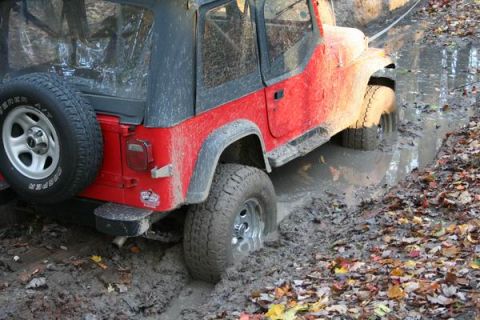 1992 Jeep Cherokee - Red Jeep Wrangler navigating a difficult muddy trail during autumn.
