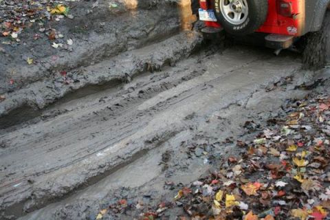 1992 Jeep Cherokee - Red Jeep Wrangler navigates a muddy trail, showing its rear tire and license plate.