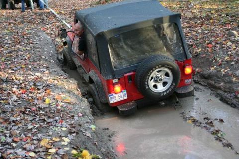 1992 Jeep Cherokee - A red Jeep Wrangler is stuck in a muddy off-road trail, with a driver looking out the window.