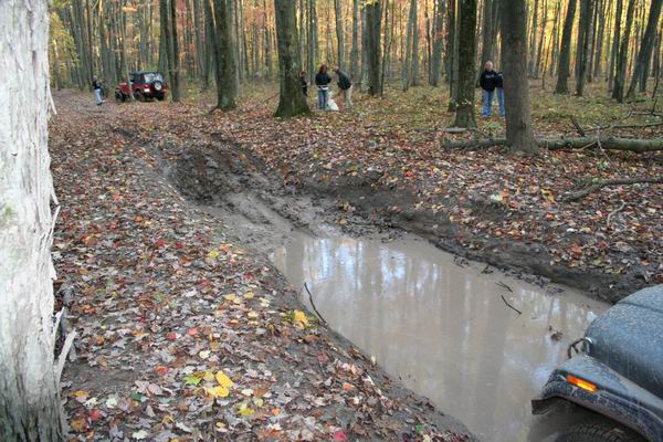 Red Jeep Wrangler on a muddy forest trail with people nearby