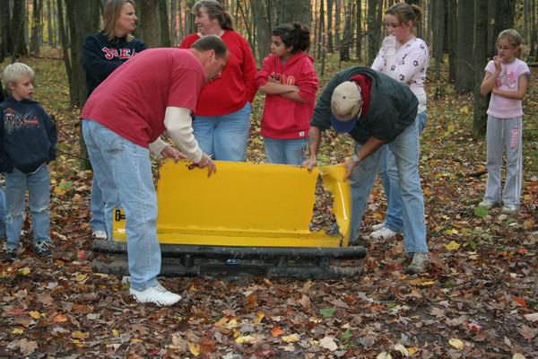 Group of people in woods removing a yellow bumper from a vehicle