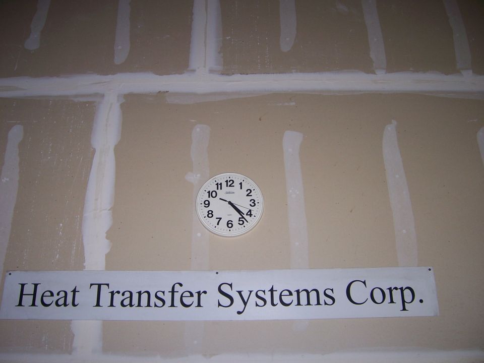 Wall with a white analog clock showing 9:45 and a sign reading "Heat Transfer Systems Corp."