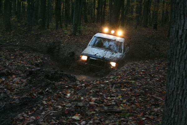 White 1992 Jeep Cherokee driving through mud with roof lights on