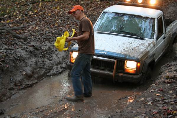1992 Jeep pickup truck stuck in mud with a person holding a yellow object
