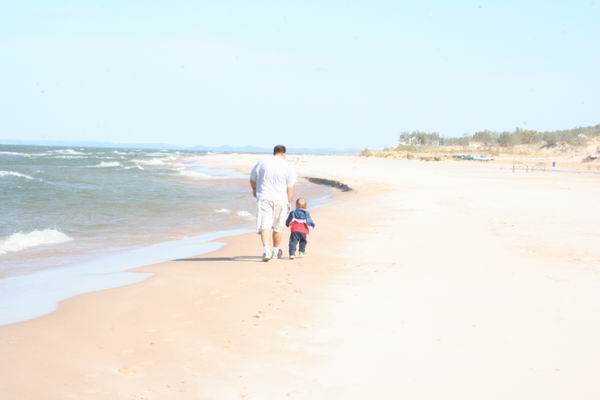 Man and kid walking on a sandy beach next to the ocean