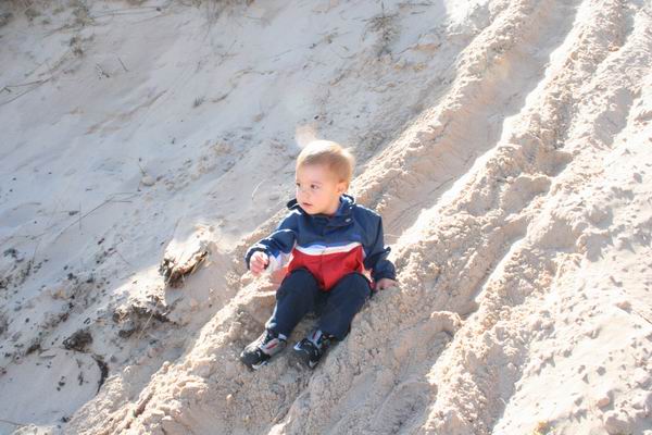 Child in blue, red, and white jacket sits on a sandy slope with tire tracks