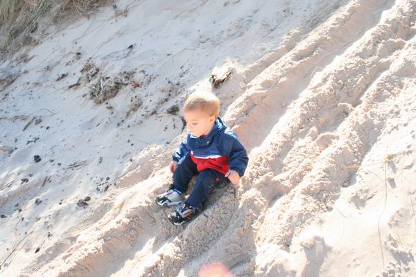 Kid sitting on a sandy slope with tire tracks