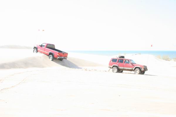 Red Jeep Cherokee and red pickup truck on sand dunes near the ocean
